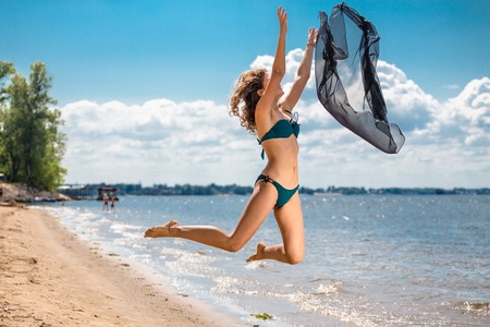 Jumping happy girl on the beach,  fit sporty healthy sexy body in bikini, woman enjoys wind, freedom, vacation, summertime fun conceptの写真素材