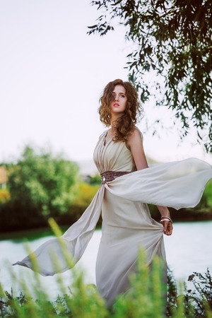 female model in long beige  dress posing dynamic in the beach. waving fabric. fluttering long skirtの写真素材