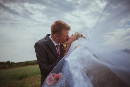 Beautiful bride and groom standing in grass and kissing. Wedding couple fashion shoot.の写真素材