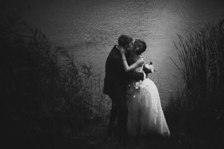 Young attractive bridal couple  holding hands outdoors next to tree by lakeの写真素材