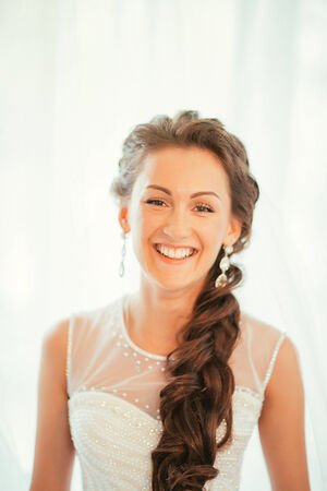 Beautiful young bride with  wedding makeup and hairstyle in bedroom, newlywed woman final preparation for wedding. Happy Bride waiting groom. Marriage Wedding day moment. Bride portrait soft focusの写真素材