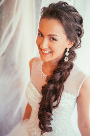 Beautiful young bride with  wedding makeup and hairstyle in bedroom, newlywed woman final preparation for wedding. Happy Bride waiting groom. Marriage Wedding day moment. Bride portrait soft focusの写真素材