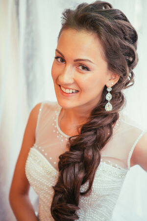 Beautiful young bride with  wedding makeup and hairstyle in bedroom, newlywed woman final preparation for wedding. Happy Bride waiting groom. Marriage Wedding day moment. Bride portrait soft focusの写真素材