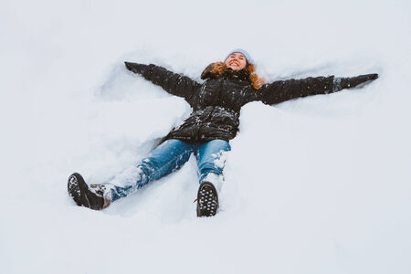 Portrait of a beautiful young woman  laying down on a frozen snow lake moving her arms and legs up...