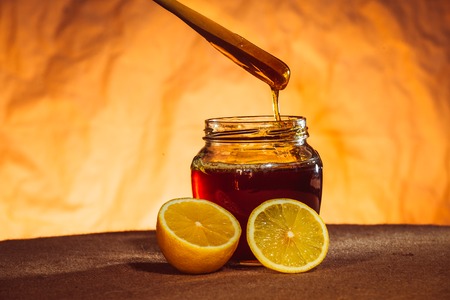 Honey jar with spoon, lemon and flowing honey, canvas backgroundの写真素材