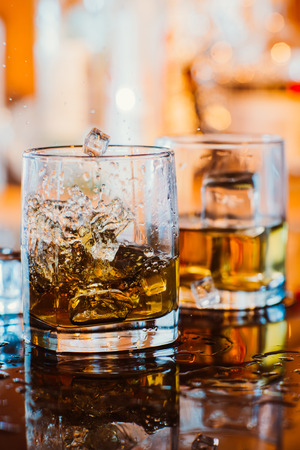 whiskey glass with ice and  warm light on black table with reflection, warm atmosphereの写真素材