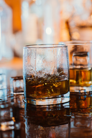 whiskey glass with ice and  warm light on black table with reflection, warm atmosphereの写真素材