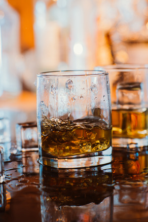 whiskey glass with ice and  warm light on black table with reflection, warm atmosphereの写真素材