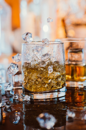 whiskey glass with ice and  warm light on black table with reflection, warm atmosphereの写真素材