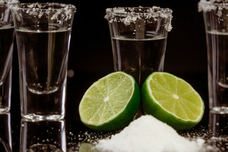 Tequila with lime and salt on black background