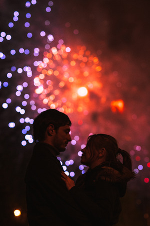 A silhouette of a kissing couple in front of a huge fireworks display. Filtered image with grainの写真素材