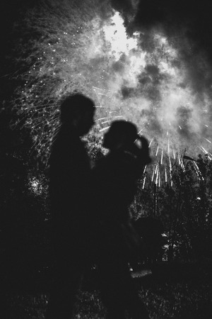 A silhouette of a kissing couple in front of a huge fireworks display. Filtered black and white image with grainの写真素材