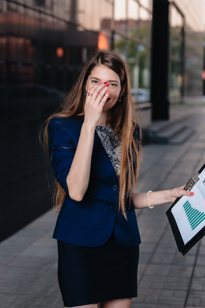 Successful businessman, standing against the backdrop of buildings holding   folder with sales charts. City business woman working.の写真素材