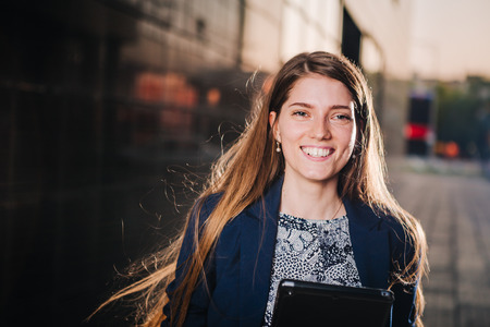Successful beautiful young business woman is smiling on the background of buildings  and holding a tablet computer.の写真素材