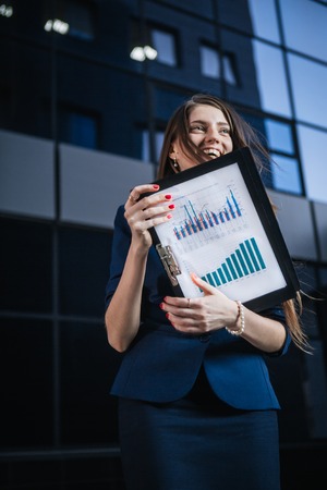 Successful beautiful young business woman standing against a background  of buildings and holding...