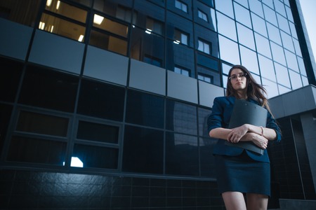 Successful beautiful young business woman standing against a background of  buildings and holding folder.の写真素材