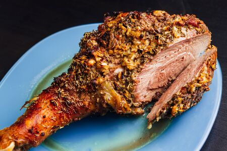 great fresh baked turkey  leg and sliced piece sprinkled with spices lying on a blue plate to black wooden backgroundの写真素材