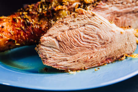 great fresh baked turkey  leg and sliced piece sprinkled with spices lying on a blue plate to black wooden backgroundの写真素材