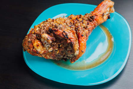 great fresh baked turkey  leg and sliced piece sprinkled with spices lying on a blue plate to black wooden backgroundの写真素材