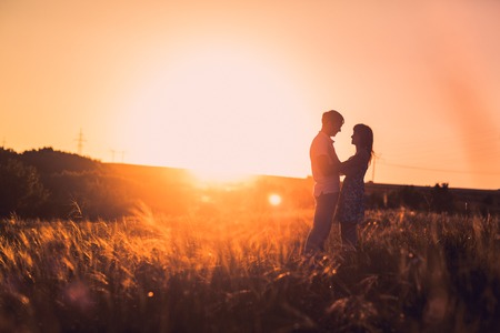 Romantic couple standing  and kissing on background summer meadow sunsetの写真素材