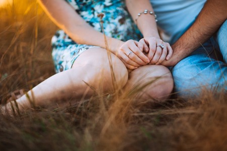 Romantic couple sit on background summer meadow sunset