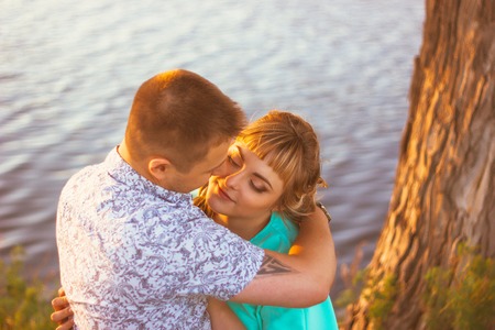 Romantic couple standing  and kissing on background summer lake sunsetの写真素材