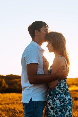 Romantic couple standing  and kissing on background summer meadow sunsetの写真素材