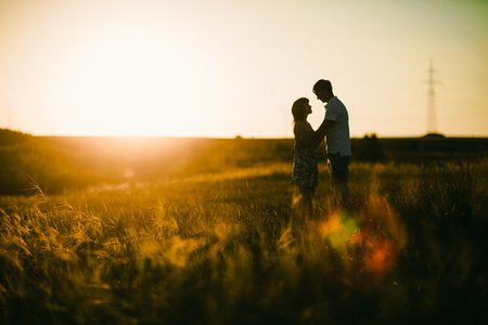 Romantic couple standing  and kissing on background summer meadow sunsetの写真素材