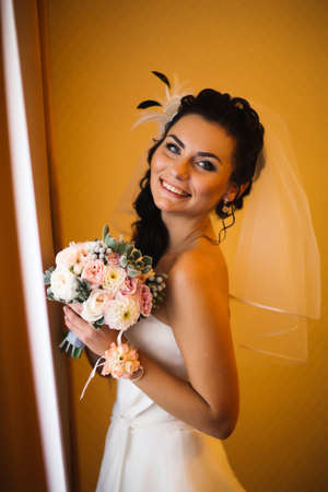 beautiful young happy bride standing near the windowの写真素材
