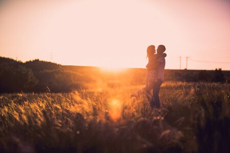 Romantic couple standing  and kissing on background summer meadow sunsetの写真素材