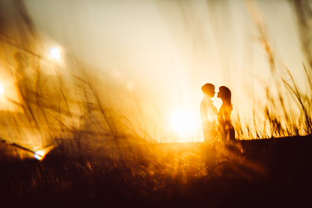 Romantic silhouette  couple standing and kissing on background summer meadow sunsetの写真素材