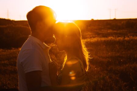 Romantic couple standing  and kissing on background summer meadow sunsetの写真素材