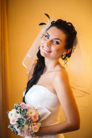beautiful young happy bride standing near the windowの写真素材