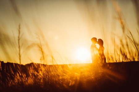 Romantic silhouette  couple standing and kissing on background summer meadow sunsetの写真素材