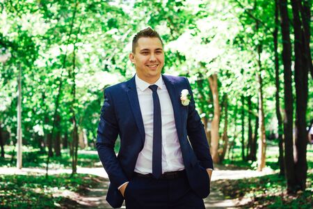 gorgeous stylish elegant happy groom standing in light on a background of beautiful sunny trees in a forestの写真素材