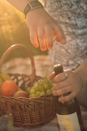 Man opening a  bottle of wine at sunset and meadowsの写真素材