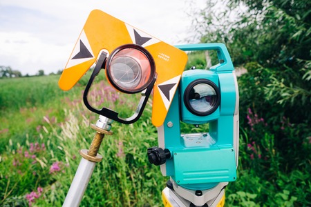 orange theodolite prism and blue surveying equipment total station on a background of lakeの写真素材