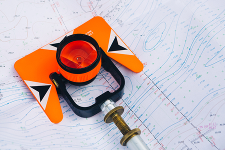 orange theodolite prism  lies on a background of geodetic maps of the areaの写真素材
