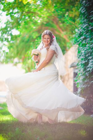 Stylish beautiful happy bride holding   bouquet of flowers on a background of trees in the summer park full lengthの写真素材