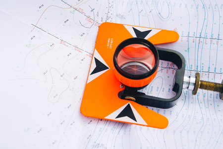 orange theodolite prism  lies on a background of geodetic maps of the areaの写真素材