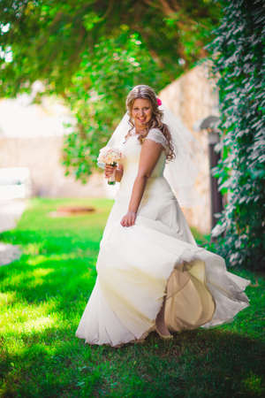 Stylish beautiful happy bride holding   bouquet of flowers on a background of trees in the summer park full lengthの写真素材