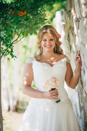Stylish beautiful happy bride holding  bouquet of flowers on a background stone wallの写真素材