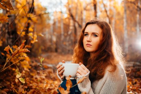 Young woman in a sweater and jeans relaxing drink tea on autumn  background