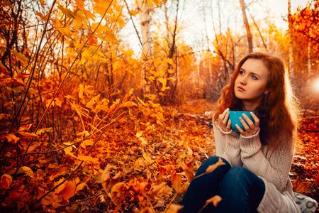 Young woman in a sweater and jeans relaxing drink tea on autumn  backgroundの写真素材