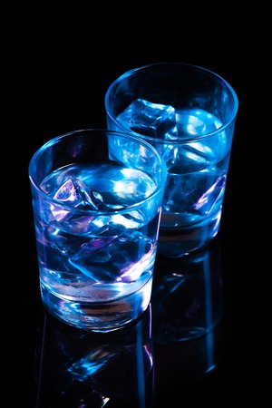 Two glasses with vodka and ice cubes against the background of deep blue glow on  dark mirrorの写真素材