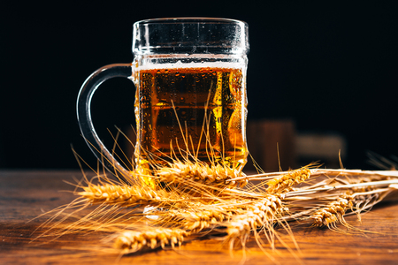 close-up  mug of light beer with ears of wheat on the wooden tableの写真素材