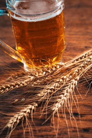 close-up  mug of light beer with ears of wheat on the wooden tableの写真素材