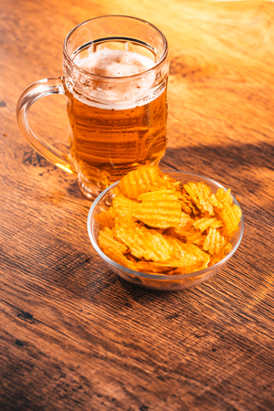 light beer mug with a bowl of potato chips on  a wooden tableの写真素材