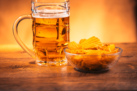 light beer mug with a bowl of potato chips on  a wooden tableの写真素材