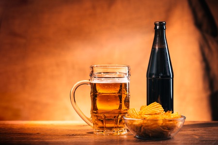 glass of fresh  light beer, a bottle beer and chips on a wooden tableの写真素材